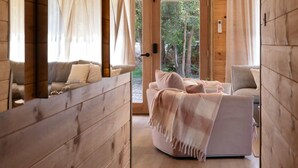 Une pièce chaleureuse avec un canapé et un fauteuil, des murs en bois et une porte vitrée donnant sur l’extérieur.