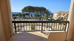 A balcony with a wooden table and white chairs, overlooking a coastal area with trees and buildings.