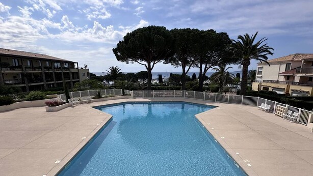 A rectangular swimming pool with a clear blue water surface, surrounded by a white fence and a paved deck.