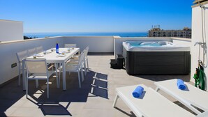 Une terrasse sur le toit avec une table dressée pour le dîner, un jacuzzi et des chaises longues avec des serviettes.