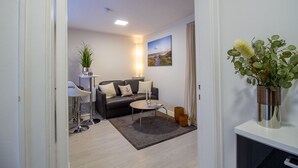 Una sala de estar moderna con un sofá de cuero negro, una mesita redonda, una planta en maceta y un cuadro en la pared.