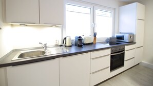 Una cocina moderna con armarios blancos, un lavamanos de acero inoxidable, un tostador, un hervidor y un microondas.