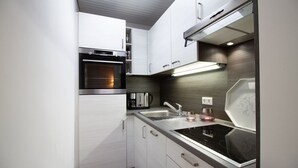 A modern kitchen with white cabinetry, a built-in oven, a stainless steel sink, and a glass-top stove. - Ostsee Lodge - Ostsee Lodge: Behaglich, Einzigartiger Meerblick & Perfekt zum Entspannen (Schashagen)