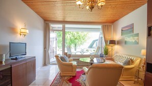 A spacious living room with a large window, a sofa, two armchairs, a coffee table, and a television on a wooden cabinet. - Ostsee Lodge - Ostsee Lodge: Behaglich, Einzigartiger Meerblick & Perfekt zum Entspannen (Schashagen)