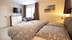 Una camera da letto con un letto, una scrivania, una sedia, una televisione e una finestra con tende.