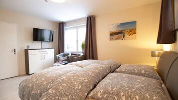 A bedroom with a bed, a desk, a chair, a television, and a window with curtains.