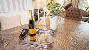 Un tavolo con una bottiglia di champagne Veuve Clicquot, due bicchieri da vino, una candela bianca e una pianta in vaso con fiori rosa.
