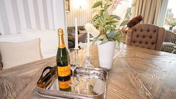 A table with a bottle of Veuve Clicquot champagne, two wine glasses, a white candle, and a potted plant with pink flowers.