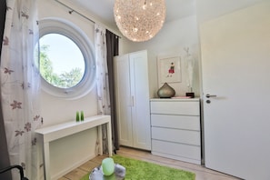 Une pièce avec une fenêtre ronde, une armoire blanche et un luminaire suspendu.