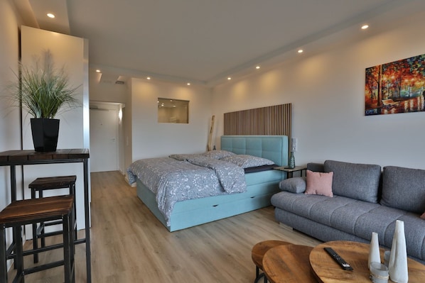 A modern bedroom with a bed, a sofa, a desk, and a potted plant.