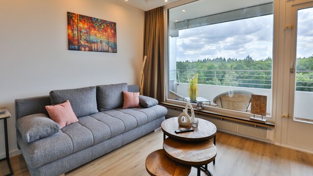 A modern living room with a grey sofa, a round wooden coffee table, and a large window with a view of greenery. - Strandkoje No. 6 - Erstklassige Lage, Ausblick, Exklusive Ausstattung für Eine Entspannte Zeit (Timmendorfer Strand)