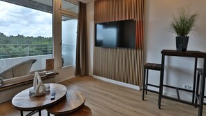 A modern living room with a large TV, a potted plant, and a balcony with a view. - Strandkoje No. 6 - Erstklassige Lage, Ausblick, Exklusive Ausstattung für Eine Entspannte Zeit (Timmendorfer Strand)