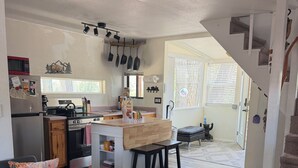 Une cuisine moderne dotée d’un îlot central, un coin repas avec un canapé et un pouf, et un escalier menant à un autre niveau.