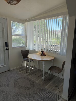 A room with a round table, two chairs, a door, and a window with vertical blinds.