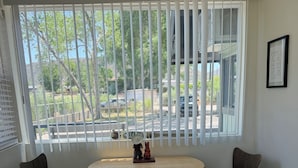 Una habitación con una mesa redonda y dos sillas, una ventana con persianas, y una alfombra en el suelo.