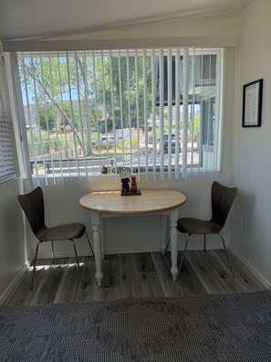 A room with a round table and two chairs, a window with blinds, and a rug on the floor.