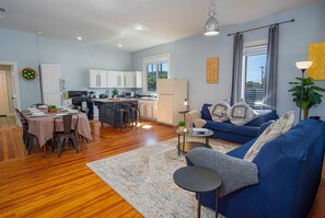 A modern living room with a blue sofa, a dining area with a table set for four, and a kitchen with white cabinets and a refrigerator. - Stunning 3BR 2BA Haven in Downtown s Heart (San Antonio)