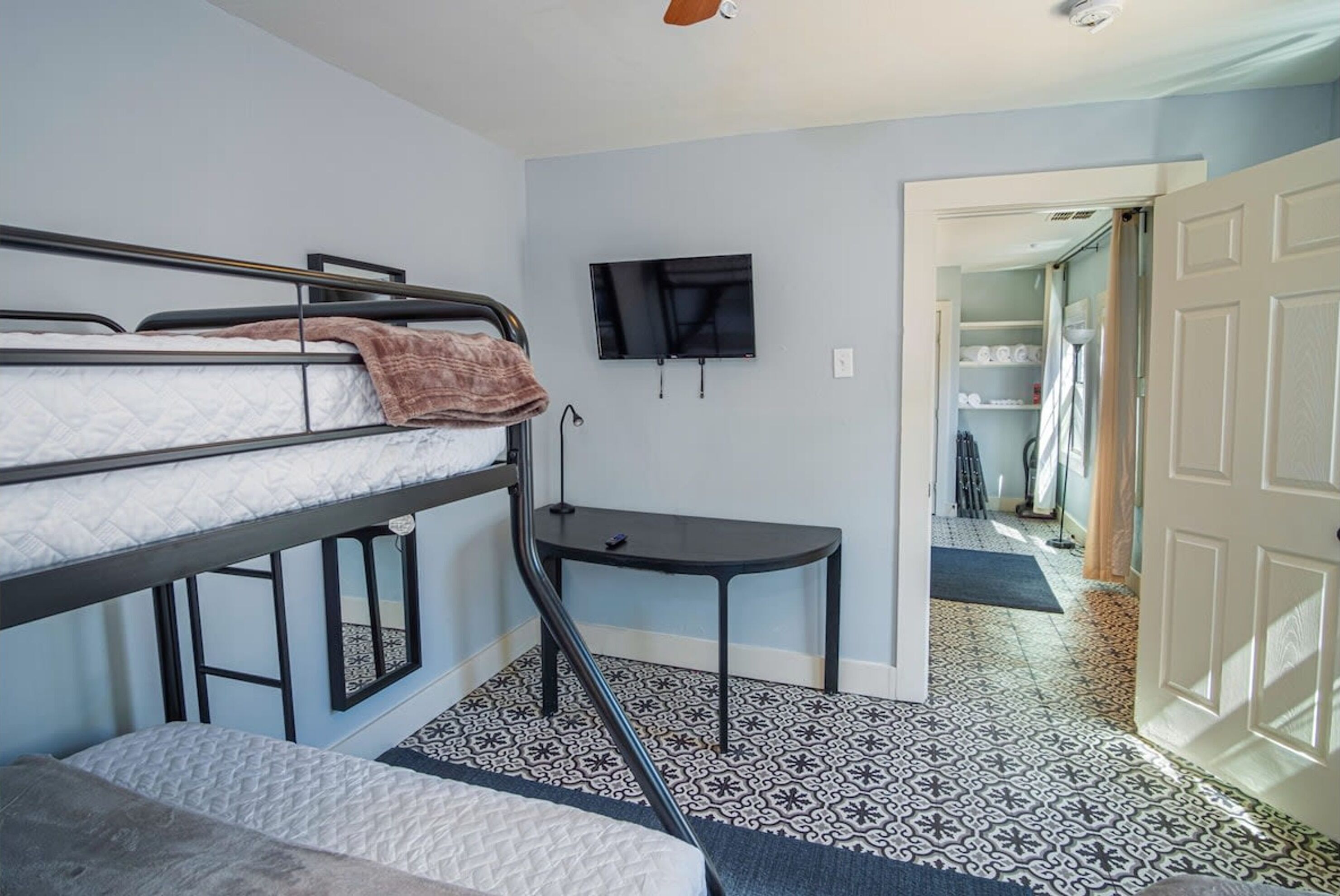 A dormitory room with bunk beds, a small table, a TV, and a patterned floor.