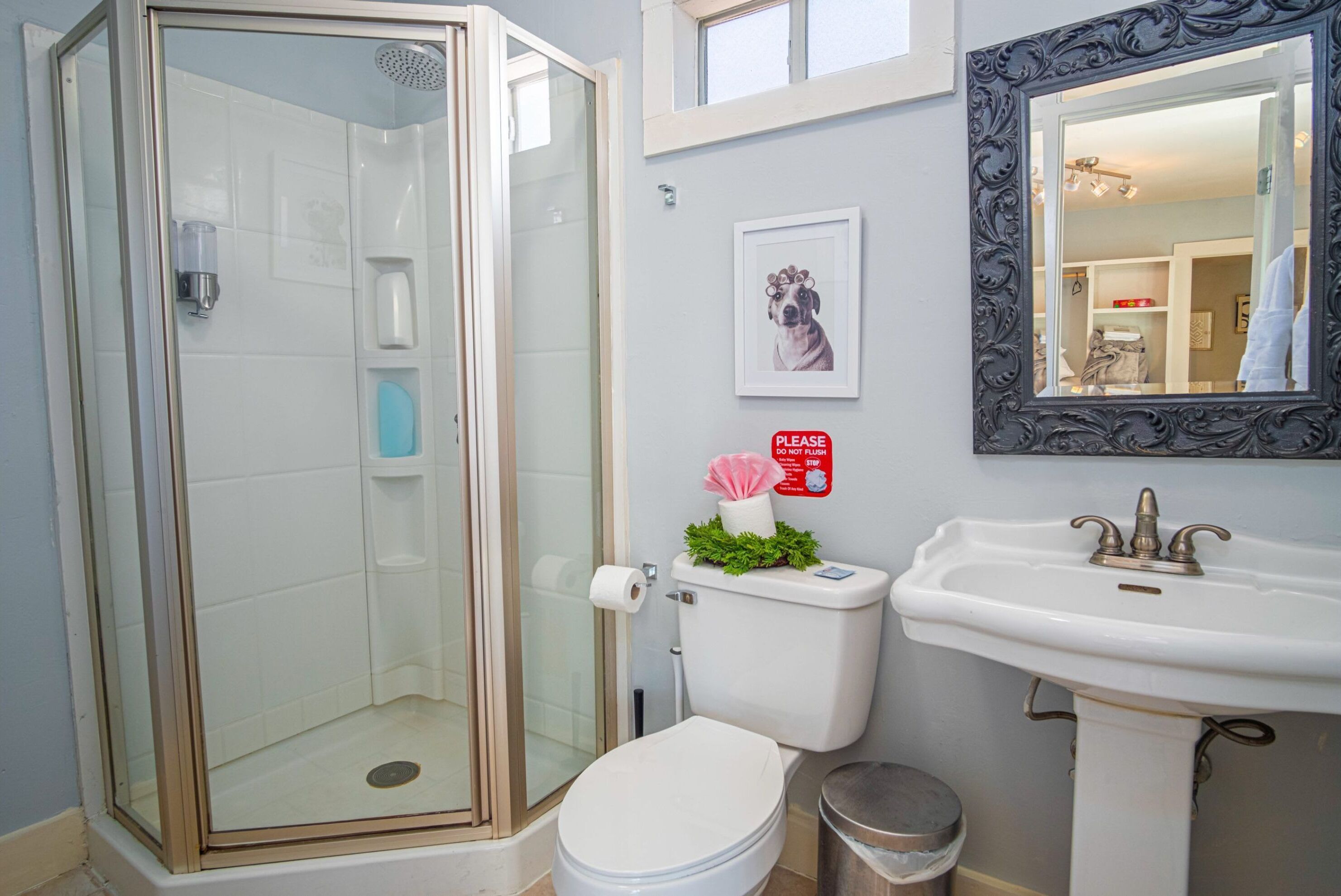 Ein Badezimmer mit einer gläsernen Duschkabine, einer Toilette mit Zimmerpflanze, einem Waschbecken und einem gerahmten Bild an der Wand.