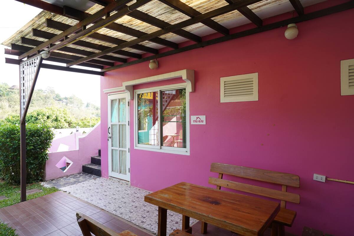Un edifici rosa amb una cadira i un taulell a l'exterior.
