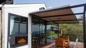 A modern house with a glass-enclosed patio area featuring wooden furniture.