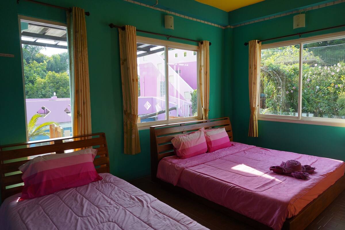 Una habitació amb dos llits, cada un amb llençol i almoadines roses, un tabernacle de fusta i una finestra amb cortines.