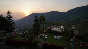 A garden with a windmill, outdoor seating, and a view of the sunset over hills. - Ban Rai Rabeangmok (Khao Kho)