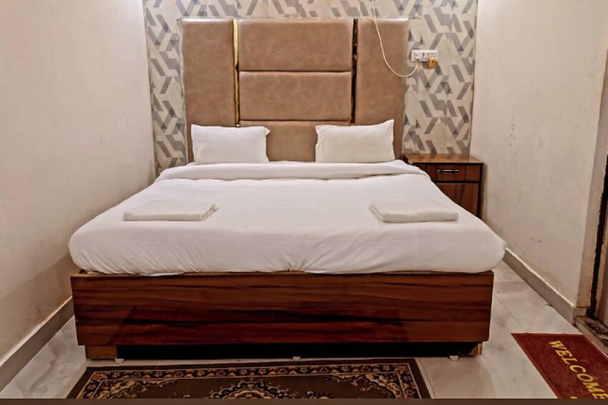 Una cama bien hecha con cabecera de madera y dos almohadas, una mesita de noche y una alfombra estampada en el suelo.