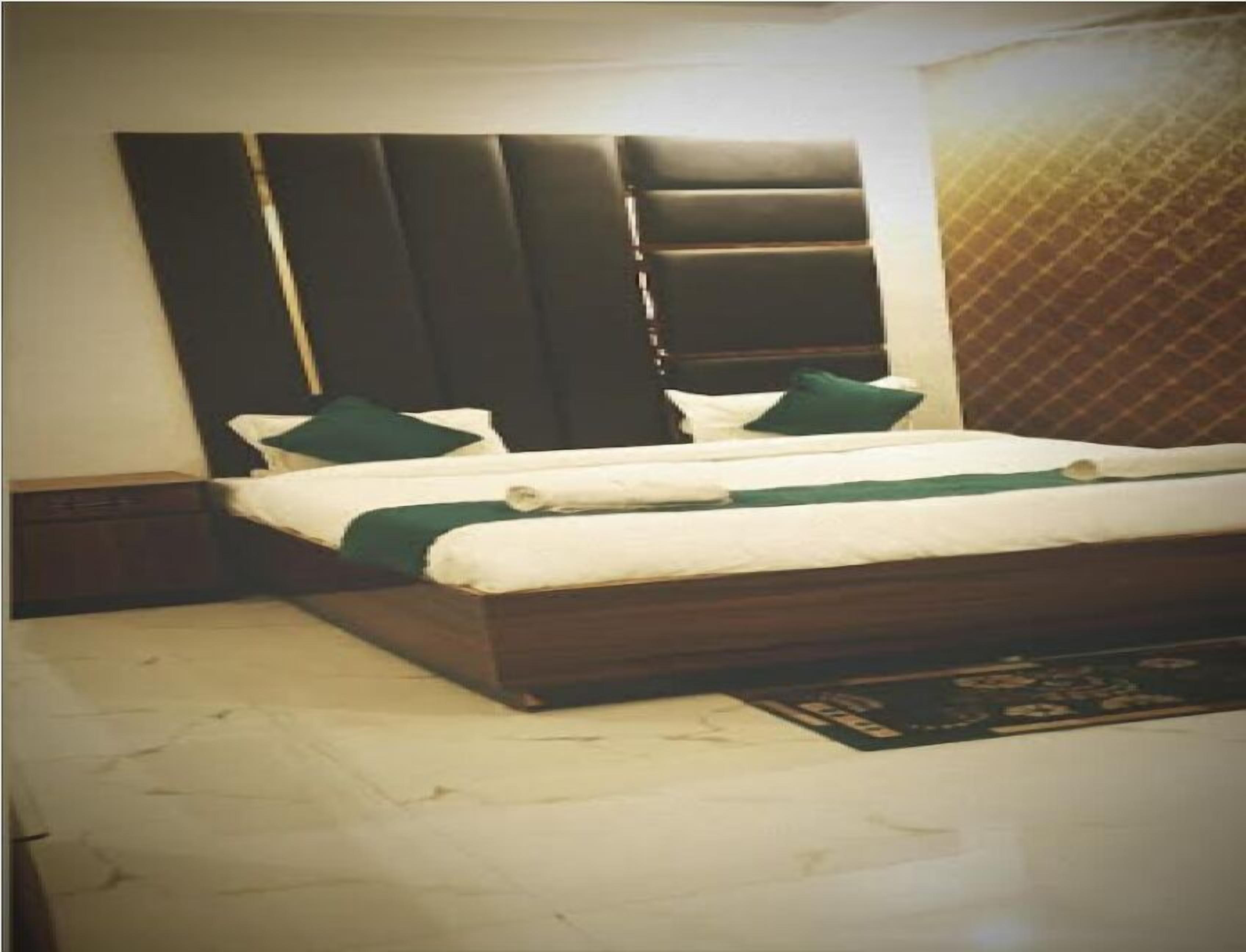 Una cama doble con cabecera oscura, dos almohadas verdes y una colcha blanca.