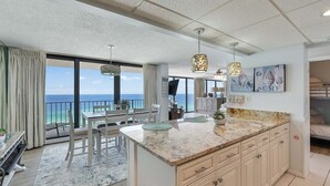 A modern kitchen with a large island, dining area with a view of the ocean, and artwork on the walls. - Edgewater T2 #911- 2 BR + Hall Bunks! (Panama City Beach)