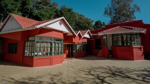 A red building with a tiled roof and large windows, surrounded by trees. - Lakefront Home Hotel (Ootacamund)