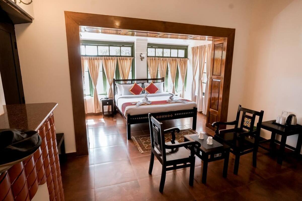 Habitación de hotel con cama, una mesa y sillas, cafetera y ventana con cortinas.
