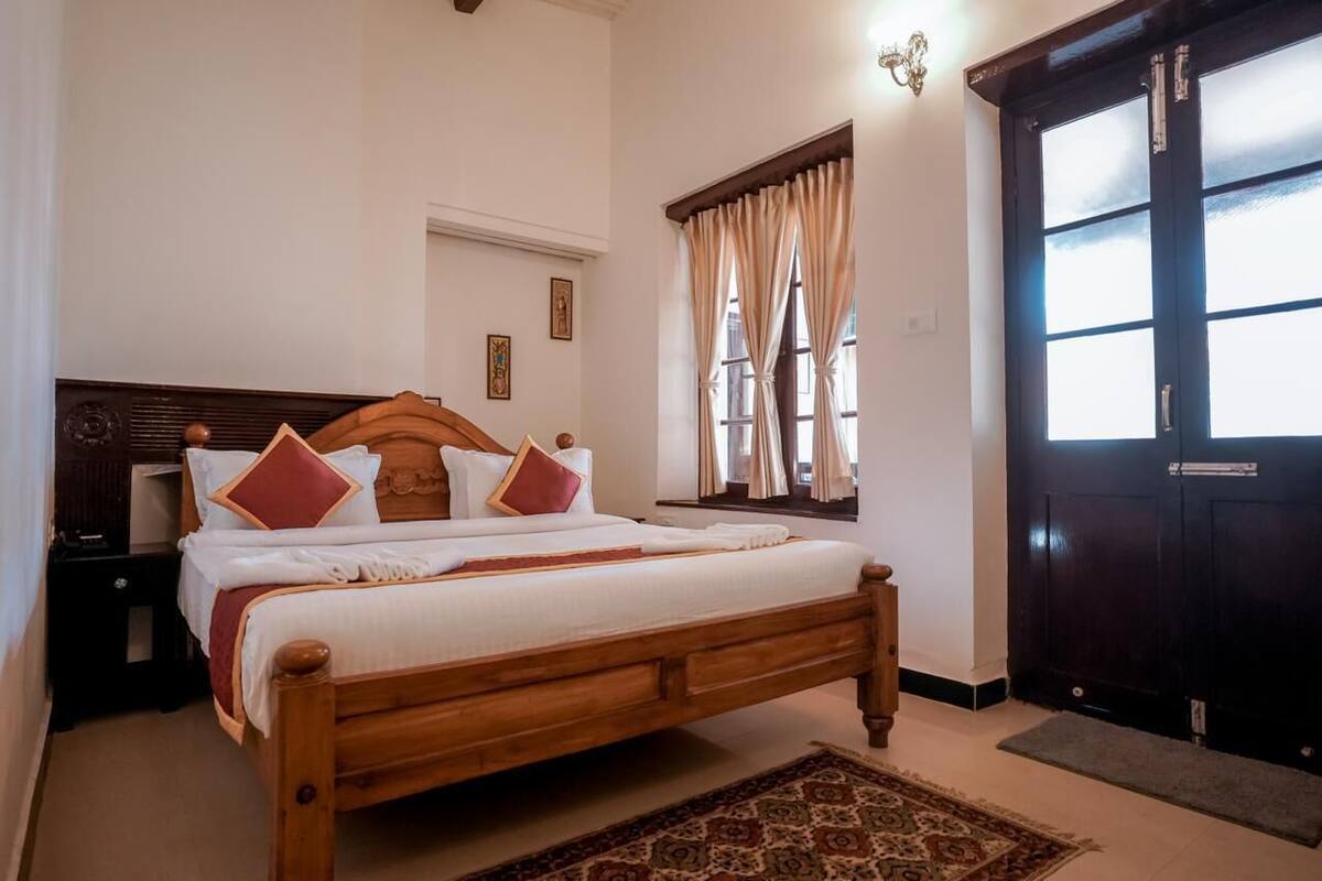 Una cama bien hecha con cabecera de madera, una mesita de noche y una ventana con cortinas.
