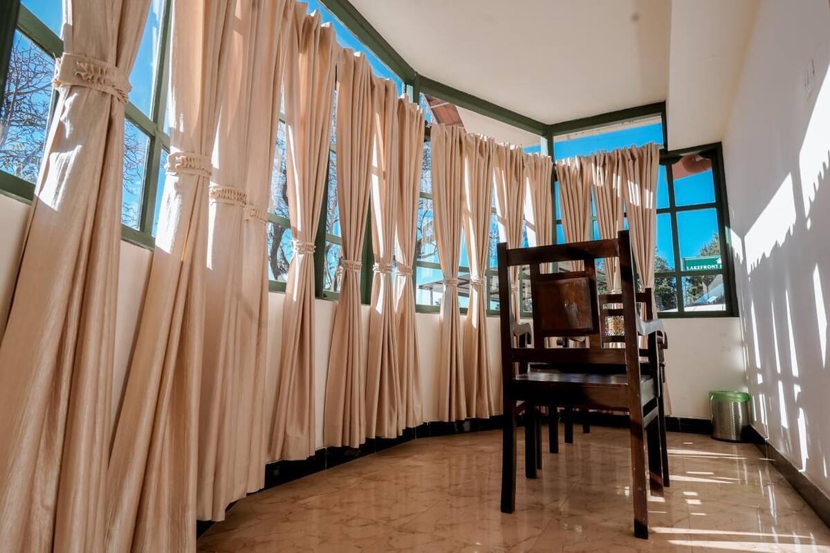 Una habitación con ventanas amplias, una silla de madera y suelo de baldosas.