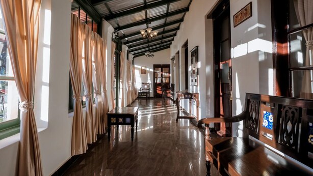 A hallway with a high ceiling, wooden flooring, and a series of windows with curtains. - Lakefront Home Hotel (Ootacamund)