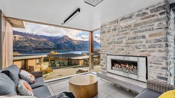 Un salon moderne doté d’une cheminée en pierre, d’une grande fenêtre offrant une vue sur les montagnes et d’un coin salon confortable.