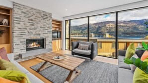 Un salon moderne avec une cheminée en pierre, une grande fenêtre donnant sur les montagnes, un canapé et une table basse.