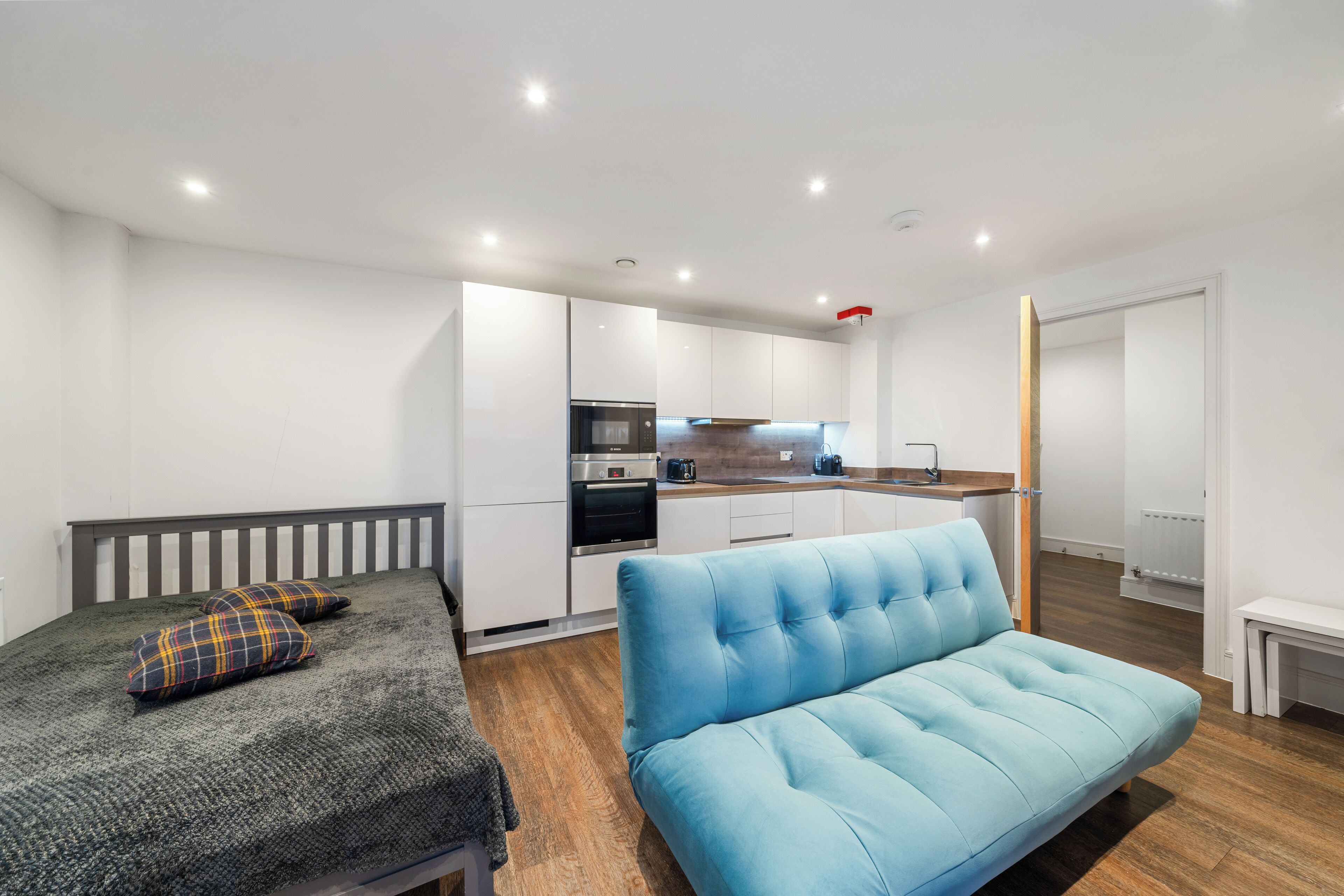 Un espacio habitable moderno y funcional con kitchenette, sofá y cama.