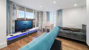 A modern living room with a flat-screen TV, a sofa, a dining table, and a bed. - Modern 1-Bedroom Flat in Central London (London)