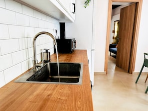 Una cocina con un lavamanos de acero inoxidable, encimera de madera y salpicadero de azulejos blancos.