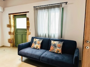 Quarto com sofá azul, porta verde e janela com cortinas leves.