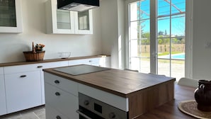 Una cocina moderna con muebles blancos, encimera de madera y un amplio ventanal con vista a una piscina.