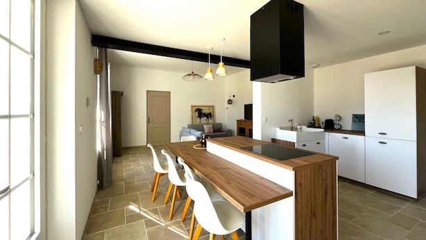 Una cocina moderna con una isla central, armarios blancos y una zona de comedor con sillas blancas.