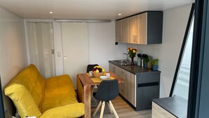 A compact living space with a sofa, a dining table, a kitchen area, and a view through a window. - Boat 'Hausboot Explorer' with Lake View and Private Terrace (Schwerin)