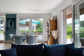 A modern living room with a dining area, large windows, and a view of the outdoors.
