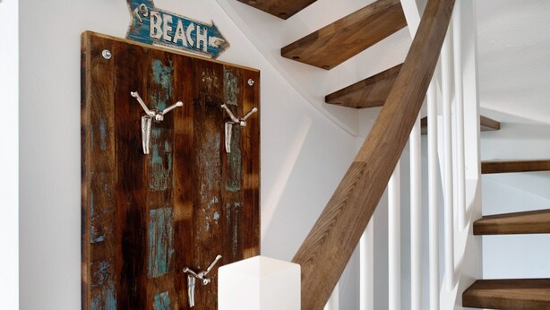 Una puerta de madera con ganchos metálicos rústicos y un letrero que dice 'BEACH' encima.