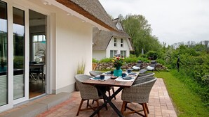 Un espacio de comedor al aire libre con sillas de mimbre, una mesa dispuesta con platos y un jarrón de flores.