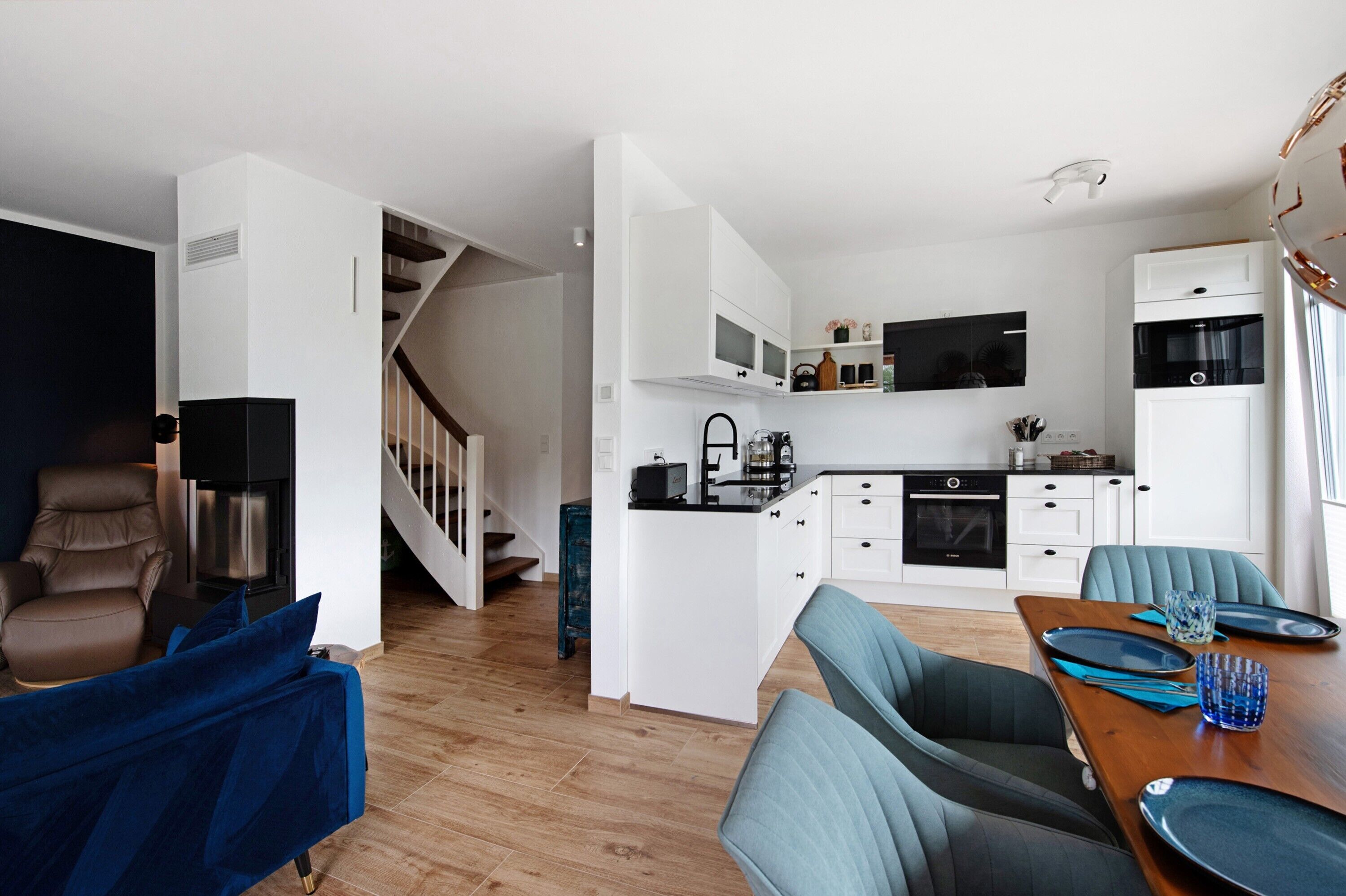 Una cucina moderna con mobili bianchi, forno a incasso e zona pranzo con tavolo in legno e sedie blu.