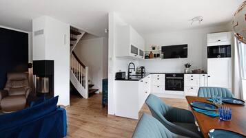 Una cucina moderna con mobili bianchi, forno a incasso e zona pranzo con tavolo in legno e sedie blu.