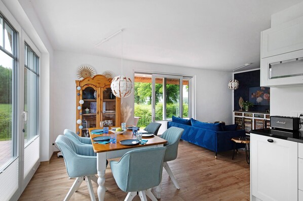 A modern kitchen with a dining area, a blue sofa, and a large window.